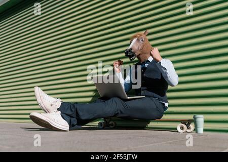 Imprenditore maschile con computer portatile indossando maschera di cavallo mentre gesturing contro parete Foto Stock