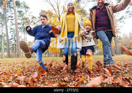 Sorridente famiglia che gioca con foglie cadde mentre cammina nella foresta Foto Stock