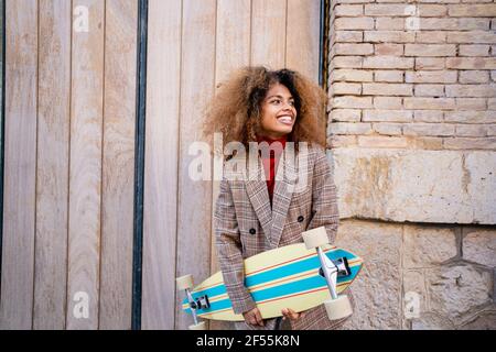 Giovane donna allegra con skateboard in piedi contro il muro Foto Stock
