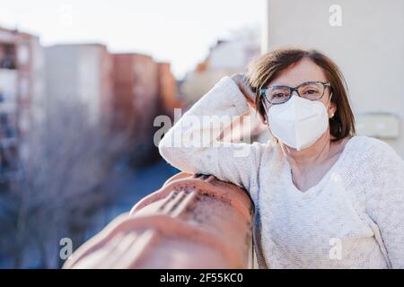 Donna anziana con testa in mano appoggiata sulla ringhiera balcone a casa durante COVID-19 Foto Stock