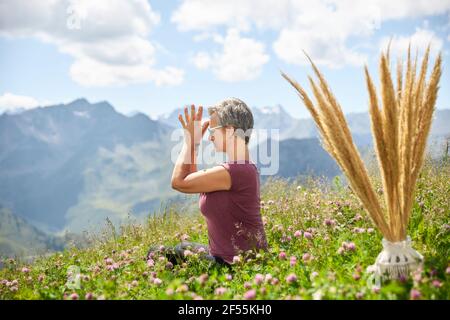 Donna attiva con mani aggrappate meditando tra piante contro il cielo Foto Stock