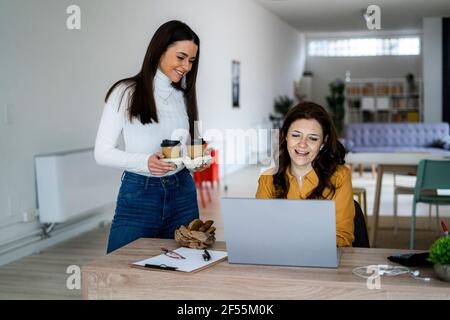 Donna sorridente che serve caffè a madre che lavora a casa Foto Stock