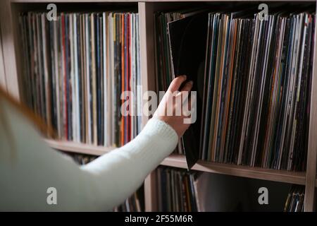 Donna che raccoglie record dallo scaffale presso il negozio di musica Foto Stock