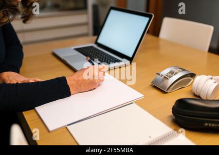 Donna con computer portatile che scrive in carta mentre lavora a casa Foto Stock