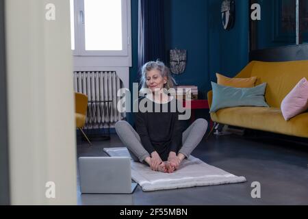 Donna anziana che fa yoga con tutorial online su computer portatile a. casa Foto Stock