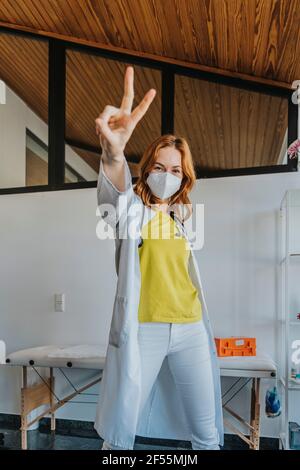 Medico gesturing segno di vittoria mentre in piedi in clinica Foto Stock