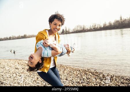 Donna felice che porta il figlio mentre si gioca sul lago al sole giorno Foto Stock