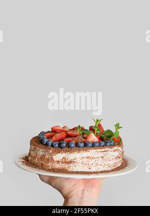 Gustosa torta fatta in casa con mascarpone decorato frutti di bosco, menta, fragole e mirtilli in mano. Formato verticale. Compleanno. Foto Stock