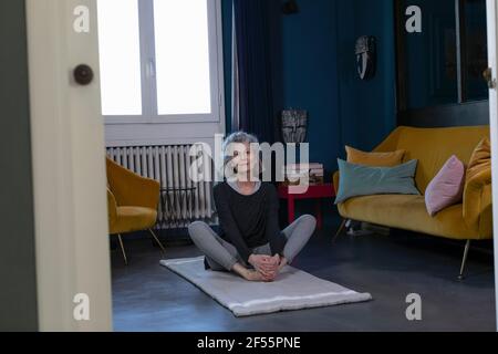 Donna anziana che pratica lo Yoga sul tappetino da ginnastica a casa Foto Stock