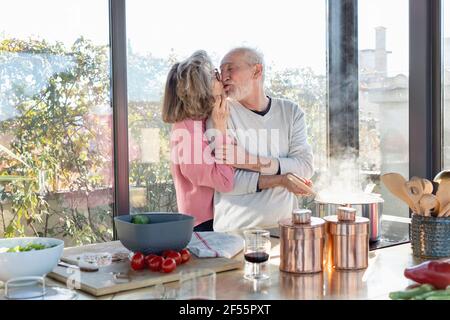 Coppia senior baciarsi mentre si sta in piedi da isola cucina a casa Foto Stock