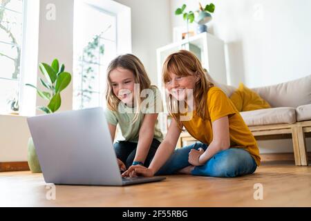 Sorridendo le ragazze che usano il computer portatile mentre si siedono a casa Foto Stock