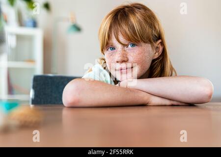 Sorridente ragazza rossa con gli occhi blu seduti al tavolo dentro soggiorno Foto Stock