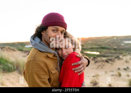 Ragazzo sorridendo mentre abbracciava la ragazza in piedi contro il cielo Foto Stock