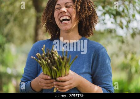 Donna ridente che tiene asparagi verdi freschi nel giardino della permacultura Foto Stock