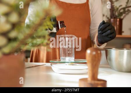 Donna che versa acqua nel bicchiere di vetro mentre fa il sapone dentro officina Foto Stock