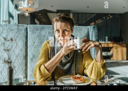 Donna con gli occhi grigi che ha il caffè al tavolo dell'hotel Foto Stock