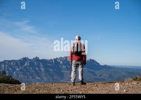 Escursionista senior con zaino che ammira la vista di Montserrat mentre si trova sulla montagna a Sant Llorenc del Munt i l'Obac, Catalogna, Spagna Foto Stock