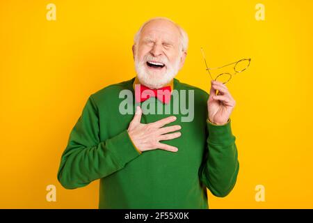 Foto di scioccato ridere età gentiluomo usura maglione bowtie tenuta occhiali chiusi occhi isolati di colore giallo sfondo Foto Stock