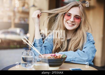 Foto all'aperto di divertente donna attraente con capelli giusti, sognando di diventare blogger di moda, in piedi in asia Street food ristorante, mangiare soba con Foto Stock