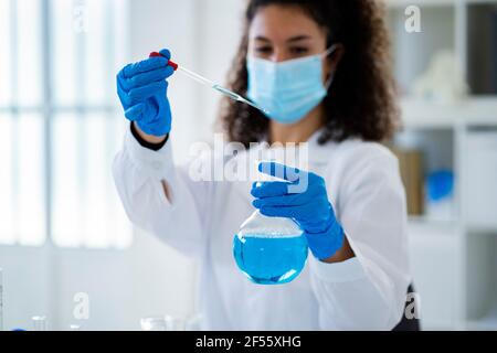 Giovane dottoressa che esamina la soluzione chimica in ospedale durante la pandemia Foto Stock