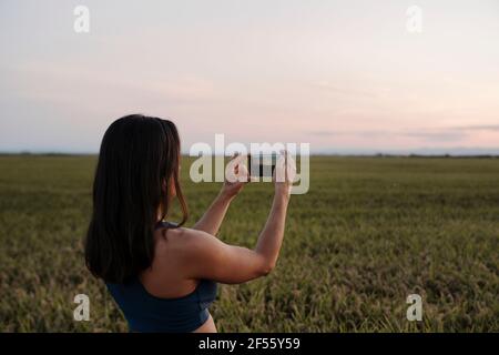 Donna che scattano foto attraverso il telefono cellulare mentre si è in piedi al prato Foto Stock