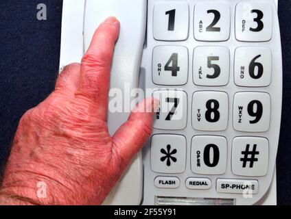 La mano di un uomo anziano o anziano prende il microtelefono di un telefono fisso grande tasto che è rivolto agli utenti anziani, disabili e ipovedenti Foto Stock