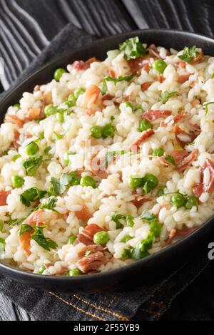 Riso italiano e Bisi riso e piselli con prosciutto primo piano in un piatto sulla tavola. Verticale Foto Stock