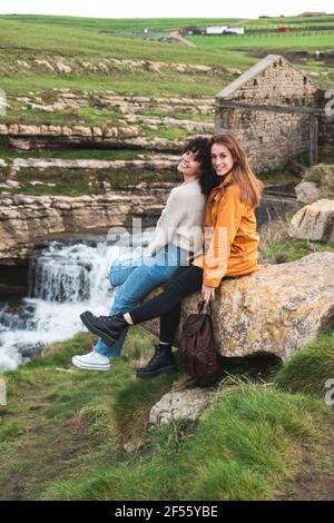 Felici amici di sesso femminile seduti sulla roccia a cascata Foto Stock