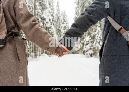 Coppia che indossa abiti caldi che tengono le mani mentre si sta in piedi nella foresta Foto Stock