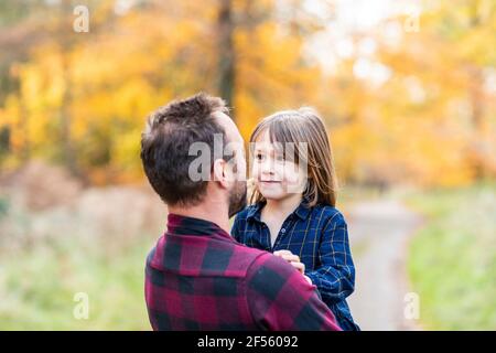 Padre che porta la figlia carina in armi mentre si trova in piedi nella foresta Foto Stock