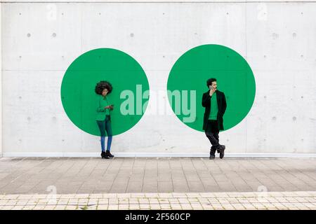 Due cerchi che visualizzano la distanza sociale che copre l'uomo e la donna in piedi in esterni con smartphone a portata di mano Foto Stock