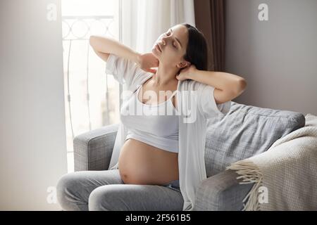 Madre grumpia stanca della sua gravidanza. Mantenere motivato rimanere da solo a casa è difficile. Alleggerendo il suo sforzo del collo e della schiena. Foto Stock