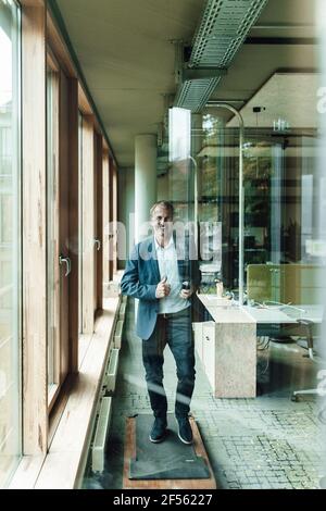 Sorridente imprenditore maschile senior che si esercita sulla pedana mobile visto trogolo di vetro finestra in ufficio Foto Stock