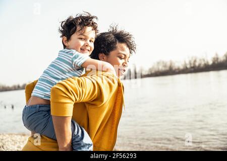 Giovane madre piggybacking figlio di lago in giornata di sole Foto Stock