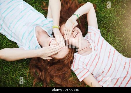 Le sorelle gemelle chiudono gli occhi dal sole, che si stendono a terra in una giornata estiva. Fooling intorno con un amico migliore è così tanto divertimento. Non c'è bisogno di andare a scuola Foto Stock