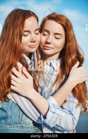 Ritratto di sorelle gemelle dai capelli rossi che si abbracciano. Le relazioni familiari e l'amicizia sono l'obiettivo della vita. Foto Stock