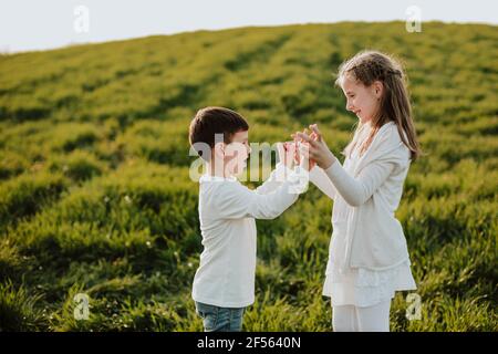 Felice ragazzo e ragazza che tiene le mani mentre si alza fianco a fianco sul prato Foto Stock