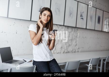 Giovane donna che ascolta la musa online sul suo smartphone che si avvicinava presto al suo posto di lavoro. Foto Stock