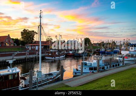 Germania, bassa Sassonia, Greetsiel, barche da pesca ormeggiate lungo il porto della città al tramonto Foto Stock