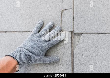 Mano di lavoro di costruzione in guanti di protezione esamina vecchio pavimento di piastrelle rotto sfondo. Concetto di rinnovamento. Foto Stock
