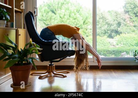 Giovane donna che si piega sulla sedia a casa Foto Stock