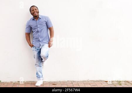 Ritratto a lunghezza intera di un giovane afroamericano sorridente che pende contro parete bianca Foto Stock