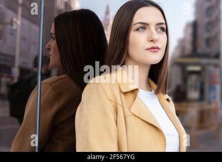 Bella donna con capelli di media lunghezza in piedi davanti parete di vetro Foto Stock