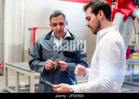 Ingegnere maschile che usa un tablet digitale mentre discute con il lavoratore fabbrica Foto Stock