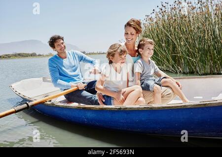 Uomo maturo che paddling mentre si siede con la famiglia in barca a remi giorno di sole Foto Stock