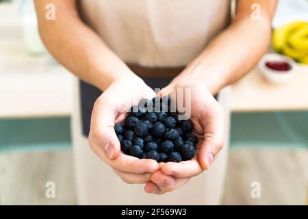 Uomo che tiene i mirtilli freschi in cucina Foto Stock