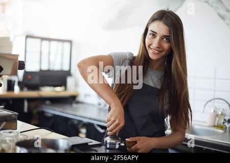 Giovane barista al lavoro guardando la macchina fotografica sorridente, utilizzando una manomissione per preparare una espresso shot. Concetto di lavoro Hipster. Foto Stock