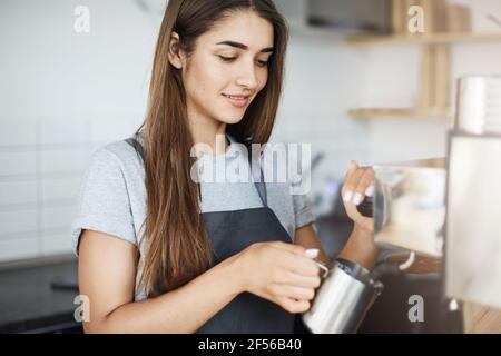 Apprendista barista signora imparando come skim latte in una caraffa il suo primo giorno in un nuovo lavoro. Foto Stock