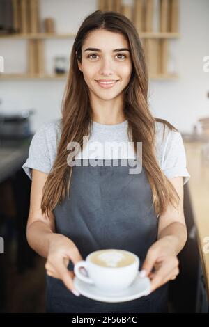 Il proprietario della caffetteria serve latte al suo primo visitatore. Foto Stock