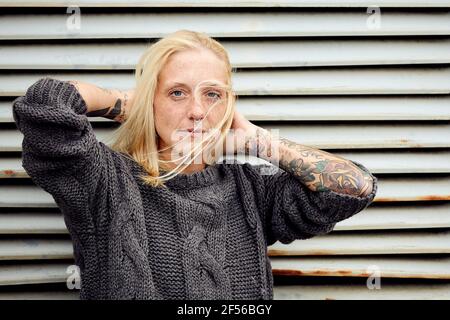 Donna tatuata con la mano in capelli in piedi davanti a. otturatore Foto Stock